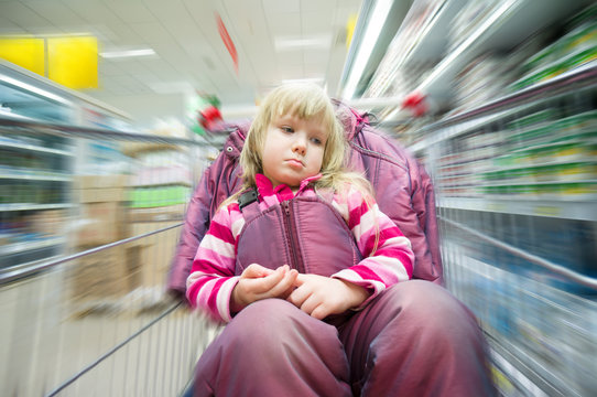 Adorable girl sit in shoping cart in milk products department in