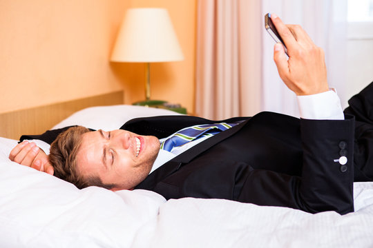 Geschäftsmann liest SMS im Hotelbett