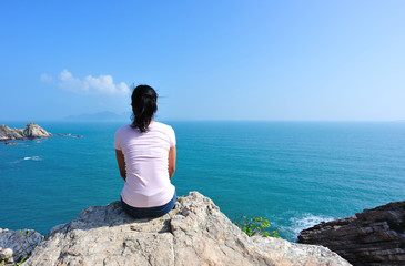Fototapeta na wymiar woman open sit on seaside rock face to blue sea
