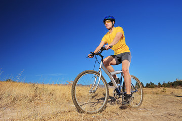 Fototapeta na wymiar A young male with yellow shirt and helmet riding a bike outdoors