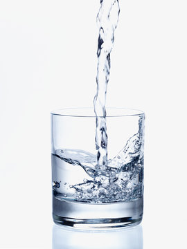 Pouring fresh water in a transparent glass, on white background