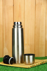 metal thermos on grass on wooden background