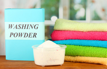 Box of washing powder with blue measuring cup and towels,