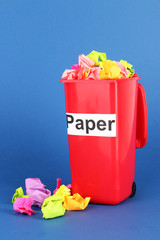 Recycling bin with papers on blue background