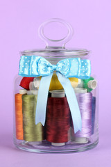 Glass jar containing various colored thread on lilac background