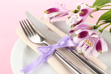 Festive dining table setting with flowers on pink background