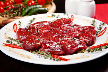 closeup of raw beef medallions with rosemary, pepper and spices