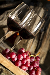 Copas de vino tinto, con uvas, botella y fuego de fondo.
