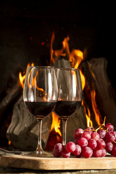 Copas de vino tinto, con uvas, botella y fuego de fondo.