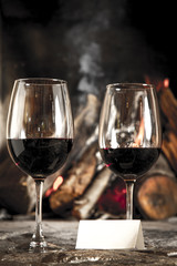 Copas de vino tinto con chimenea y fuego de fondo.