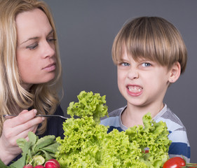 Lovely boy with his mom, refusing to eat green salad