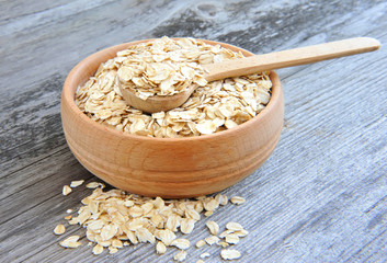 Oat flakes in bowl and wooden spoon on old wooden background