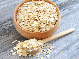 Oat flakes in bowl and wooden spoon on old wooden background