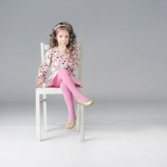 Sweet thoughtful little girl sitting on the white chair, a lot o - 51037013