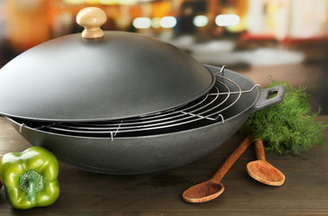 Black wok pan and vegetables on kitchen wooden table, close up