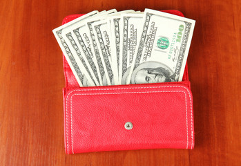 Purse with hundred dollar banknotes, on wooden background