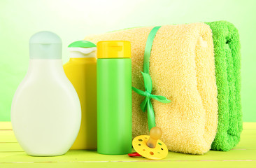 Obraz na płótnie Canvas Baby cosmetics and towels on wooden table, on green background