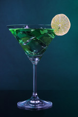 Green cocktail with lime on dark green background