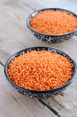 Oriental bowls with red lentils on wooden background