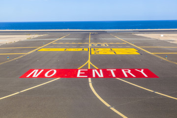 no entry sign at the runway of the airport with ocean in backgro