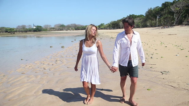 Happy couple holding by hands and walking together at beach