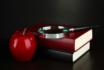 books with magnifying glass on table on black background