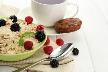 tasty oatmeal with berries and cup of tea, on white wooden