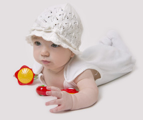 Baby in white hat playing with rattles on white background