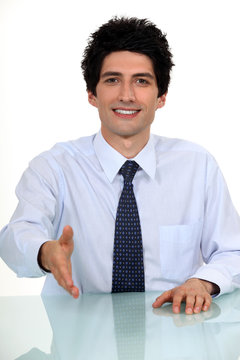 Businessman sat at desk offering to shake-hand