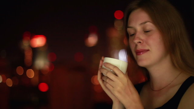 Young woman drinking coffee on night city background.