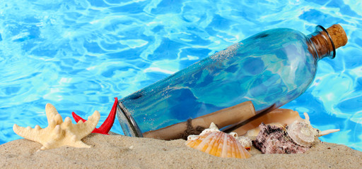 Glass bottle with note inside on sand, on blue sea background