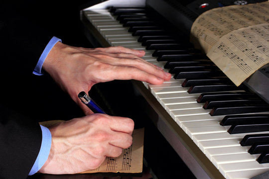 man hands playing piano and writes on parer for notes