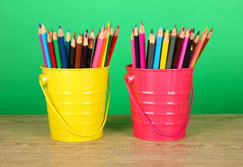 Colorful pencils in two pails on table on green background