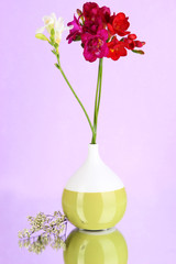 Beautiful bouquet of freesia in vase on purple background