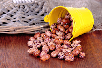 Overturned bucket with beans on wooden background