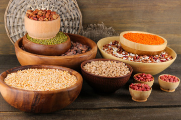Different kinds of beans in bowls on wooden background