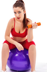 Young pretty woman lifting up dumbbells while sitting on a gym b