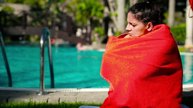 Sad woman in red towel sitting by the swimming pool, tilt up dow