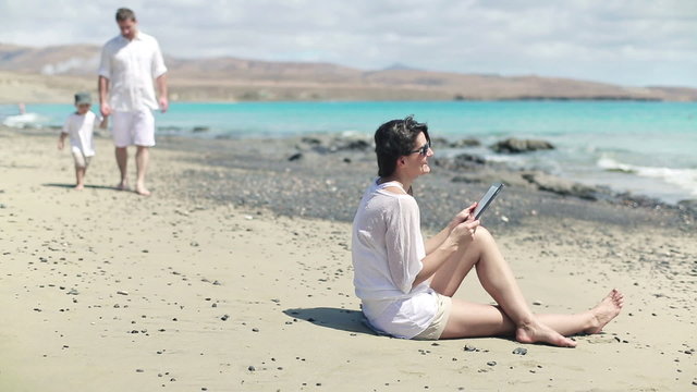 Happy family chatting with tablet computer on the beach