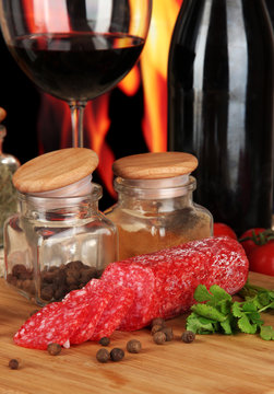 Tasty salami on board wooden table on fire background