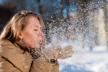 Beautiful blond young woman blowing Snow outdoors