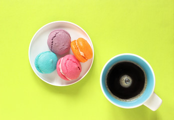 Macarons on a plate and a cup of coffee on green background