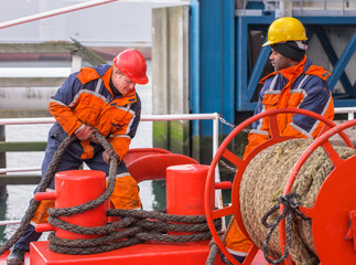 European deck officer working with ropes together with African s - obrazy, fototapety, plakaty