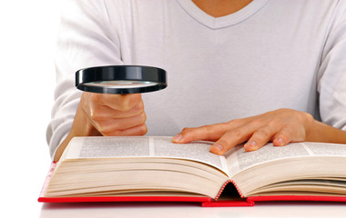 Mujer leyendo un libro sujetando una lupa.