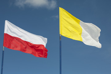 Polish and Vatican flags in the wind against a sky