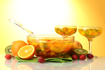 punch in bowl and glasses with fruits, on yellow background