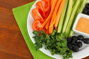 Assorted raw vegetables sticks in plate on wooden table close