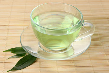 Transparent cup of green tea on bamboo mat, close up