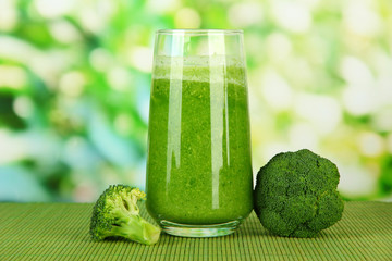 Glass of broccoli juice, on bamboo mat, on green background