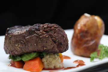 Tenderloin steak portion with potato on black background